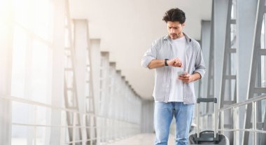 Transfer için zaman yok. Endişeli adam havaalanında kol saatine bakıyor, uçağına geç kalıyor, bavul ve akıllı telefonuyla terminalin koridorunda duruyor.