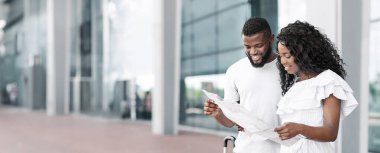 Genç siyah bir çift havaalanı terminalinde durmuş, yüzlerinde gülümsemeyle uçuş güzergahlarını gözden geçiriyorlar. Çift gündelik giysiler giyip, boş zamanlarında fotokopi çekiyorlar.