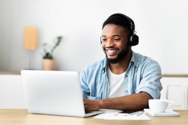 Dizüstü bilgisayarda çalışan ve kulaklıkla müzik dinleyen neşeli siyahi serbest yazar, boşluğu kopyala
