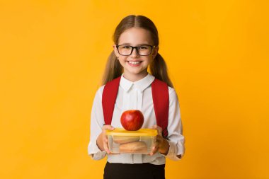 Sağlıklı Okul Yemeği. Sevimli İlköğretim Öğrenci Kız Sandviç ve Sarı Arka Plan Üzerinde Elma ile Lunchbox Holding. Kopyalama Alanı
