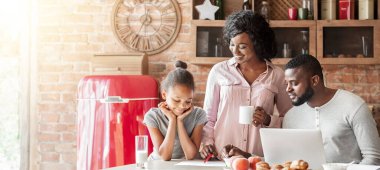Genç afro bir aile hafta sonu evde kahvaltı ediyor, dizüstü bilgisayar, çizim, boş alan kullanıyorlar.