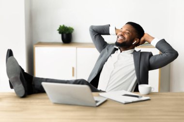 Bir işadamı masasına yaslanmış, gülümsüyor ve müzik dinliyor..