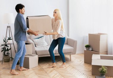 Bir çift yeni evlerinde paketlenmemiş kutularla çevrili büyük bir karton kutu taşıyor..