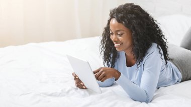Afrikalı güzel kız dijital tablet hakkında blog okuyor, yatakta yatıyor, boş yer var.