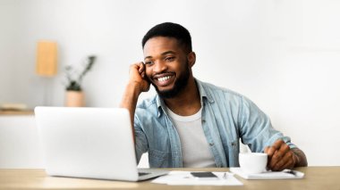 Yakışıklı genç çalışan telefonda konuşuyor ve ofiste dizüstü çalışırken kahve içerken, kopya alanı