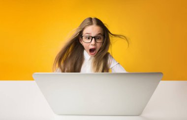 Sürpriz okul kız sarı stüdyo arka plan üzerinde dizüstü bilgisayarda ev ödevi yapıyor. Kopyalama Alanı