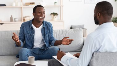 Başarılı bir terapi. Neşeli siyahi adam ofisinde buluşurken psikologla konuşuyor, ilerlemesini doktorla paylaşıyor.