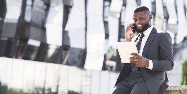 Şehir merkezinde kahve molası sırasında dijital tablet kullanan pozitif Afrikalı girişimci cep telefonuyla konuşuyor.