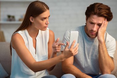 Sadakatsizlik. Kıskanç kız arkadaş, aldatan erkek arkadaşına telefonunu gösteriyor. Kapalı bir odada otururken telefonda açıklama istiyor.