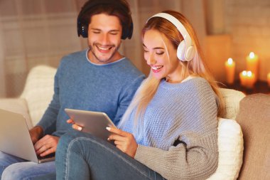 Kablosuz kulaklıklı olumlu eşler dizüstü bilgisayarda ve dijital tabletle evde akşam geçiriyorlar. Seçici Odaklanma