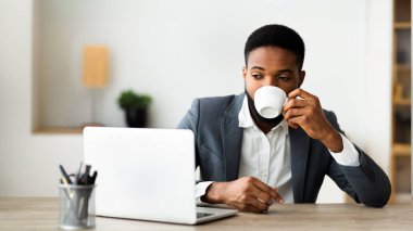 Modern ofiste dizüstü bilgisayar üzerinde çalışırken kahve içen Afrikalı Amerikalı adam, panora, bir kopya alanı ile