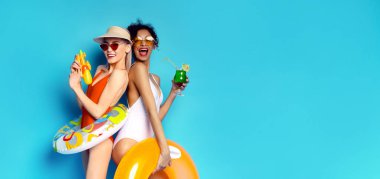 Bu görüntüde mayolu iki kadın mavi arka planda poz veriyor. İki kadın da gülümsüyor ve havuzda eğlenceli bir gün için hazır görünüyorlar.