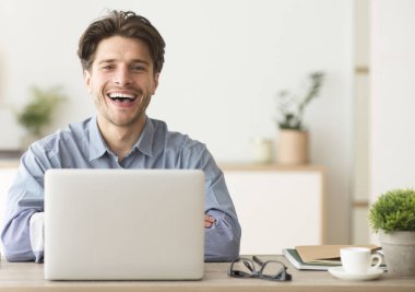 Adam dizüstü bilgisayarda oturuyor ve içerideki kameraya bakıp gülüyor. Metin için Boşluk