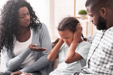 Aile eğitimi. Küçük siyah kız, ebeveynlerinin azarlamalarını dinlememek için kulaklarını kapatıyor.