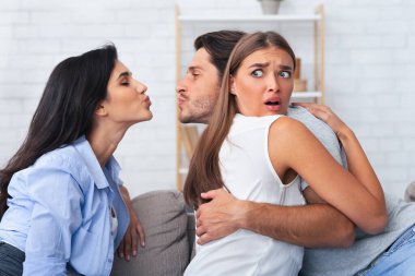 Aşk Üçgeni ve Kıskançlık. Aldatan Erkek Arkadaşı Bir Kızı Öperken Kız Arkadaşına Sarılarak Kanepede Kapalı Oturarak Birlikte Oturuyor.