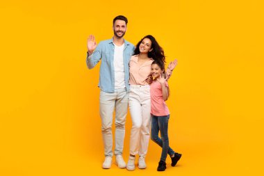 Üç kişilik mutlu bir aile, bir baba, bir anne ve bir kız, parlak sarı bir arka planın önünde duruyorlar. Hepsi gülümsüyor, el sallıyor ve eğleniyor gibi görünüyorlar..