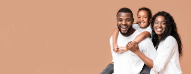 Aile eğlencesi. Genç Afrikalı Amerikalı ebeveynler küçük kızlarıyla vakit geçiriyorlar, sarı arka planda birlikte gülüyorlar.