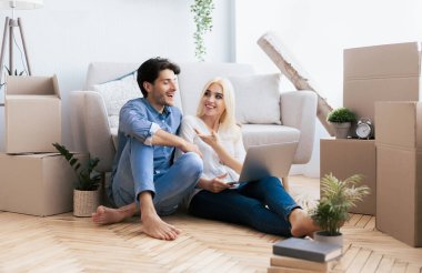 Bir çift yeni evlerinin zemininde oturuyor, paketsiz kutularla çevrili, dizüstü bilgisayar planlarken..