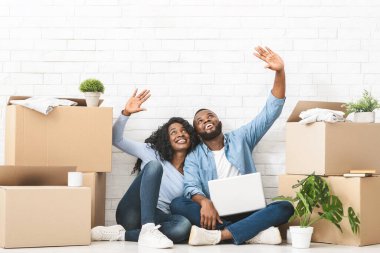 Yeni ev dekorasyonu. Genç Afrikalı çift yeni evlerinde yerde oturuyor ve dizüstü bilgisayar kullanarak fotokopi alanını işaret ediyorlar.