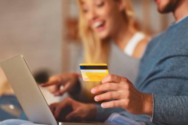 Tanınmayan bir çift dizüstü bilgisayar ve kredi kartı kullanıyor internetten evdeki koltukta oturan bir şey sipariş ediyorlar. Seçici Odaklanma, Kırpılmış