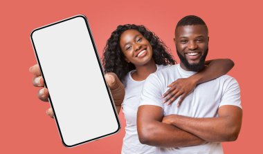 Gülümseyen siyah bir çift pembe bir arka plana karşı duruyor. Kadın elinde beyaz ekranlı bir akıllı telefon tutuyor..