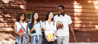 Bir grup mutlu öğrenci üniversite kampüsünde geziyor, teneffüste sohbet ediyor ve gülüyorlar.