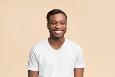 Beyaz tişörtlü neşeli siyahi adamın portresi. Sarı arka planda kameraya gülümsüyor. Stüdyo Çekimi