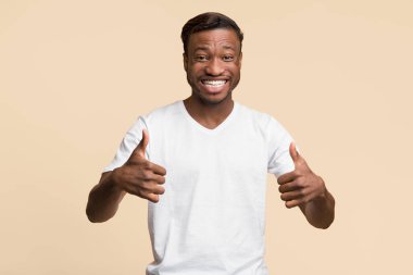 Gibi. Afrikalı Amerikalı Milenyum Adamı, Stüdyoda sarı arka planda durup kameraya gülümseyen iki eliyle başparmağını kaldırıyor.