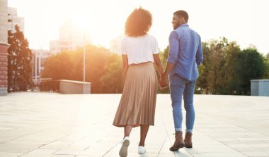 El ele tutuşan ve gün batımında şehirde yürüyen çift