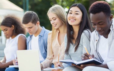 Zeki uluslararası öğrenciler, dizüstü bilgisayar ve not defterleri kullanarak parktaki final sınavlarına hazırlanıyorlar.