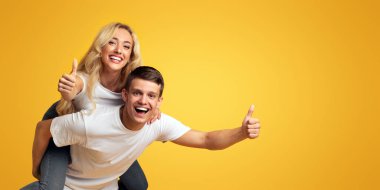 Harika bir teklif. Neşeli milenyum çifti başparmaklarını göstererek sarı stüdyo arka planında fotokopi alanı ve panorama ile birlikte eğleniyorlar.