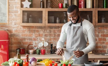 Yakışıklı gülümseyen siyah adam mutfakta taze sağlıklı salata hazırlıyor.
