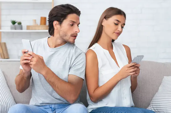 stock image Jealousy Concept. Jealous Boyfriend Reading Girlfriends Messages On Phone While She Texting Sitting On Couch At Home.