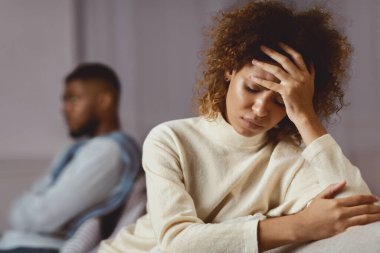 İlişki sorunları. Siyahi adam ve kadın konuşmaktan kaçınıyor, kanepenin farklı taraflarında oturuyor.