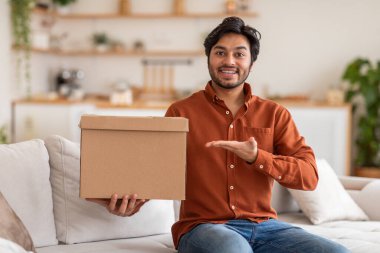 Turuncu gömlekli bir Arap kanepeye oturmuş, elinde bir karton kutu, kameraya gülümsüyor. Bir el kutuya doğru hareket ederken, diğeri kutuyu belinin önünde tutuyor..