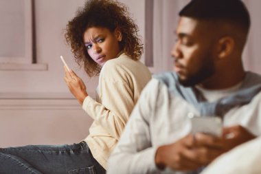 Afro kadın kocasına ihanet ettiğinden şüpheleniyor, telefonu kullanıyor ve adama bakıyor.
