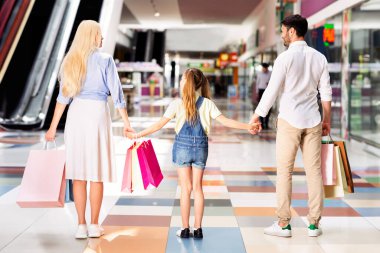Üç kişilik bir aile, bir anne, bir baba ve küçük bir kız, ellerinde çantalarla bir alışveriş merkezinde yürüyorlar. Kameradan uzaklaşıyorlar, el ele tutuşuyorlar ve ileriye bakıyorlar..