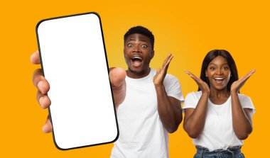 Sarı arka planda duran siyah bir çift, bir el tarafından tutulan boş bir akıllı telefon ekranına bakıyor. İkisinin de elleri heyecanla havada ve yüzlerinde kocaman bir gülümseme var..