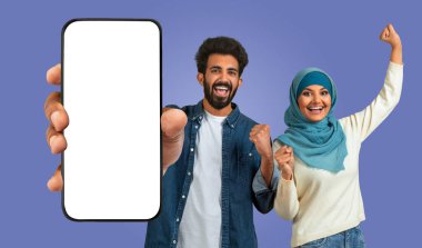 Doğu 'lu genç bir Müslüman erkek ve kadın ellerinde boş ekranlı bir akıllı telefon tutuyorlar. İkisi de gülümsüyor ve heyecanlılar. Bir şey kutluyorlar.