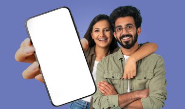Genç bir Hintli çift mavi bir arka planın önünde duruyor, ellerinde boş bir ekranla akıllı bir telefon tutuyorlar. Kadın gülümsüyor ve kolunu erkeğin omuzlarına dolamış..
