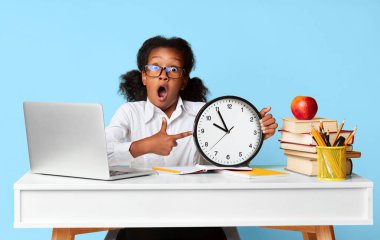 Zaman Yönetimi ve Okul Teslim Tarihi. Şok olmuş afro ilkokul öğrencisi kız, sarı arka planda dizüstü bilgisayarında oturan saati işaret ediyor..