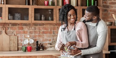 Afrika kökenli Amerikalı bir adam yemek pişirirken karısına sarılıyor, birlikte salata yapıyor, boş bir yer.