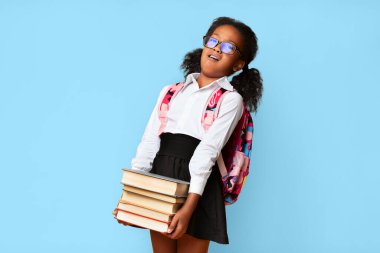 Sarı stüdyo arka planında ağır kitaplar taşıyan mutsuz afro birinci sınıf öğrencisi. Ev ödevleri çok yoğun. Boş alan