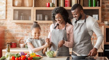 Genç afro ebeveynler kızlarına sebze salatası yapmayı öğretiyor. Mutfak içi, içi boş panorama.