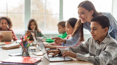 Teacher Teaching Diverse School Kids Using Laptop In Classroom. African American Schoolboy And Diverse Classmates Browsing Internet On Computer Learning Online Indoor. E-Learning Concept