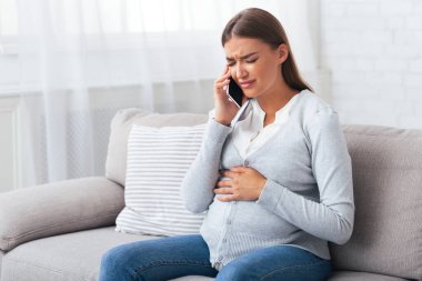 Acil durum çağrısı. Hamile Kız Evde Kanepede Oturan Ağrı Kötü Acı Feeling Cep Telefonu On Talking.