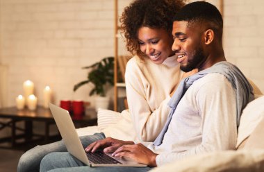 Genç evli çift sıcak kış akşamında dizüstü bilgisayar kullanıyor, evde dinleniyor, boş yer var.