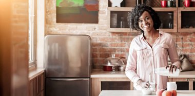 Gülümseyen siyah kadın mutfakta tek başına kahvaltı yapıyor, bardağa süt döküyor, sağlıklı kahvaltı konsepti, kopyalama alanı.