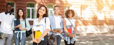 Geleceğin profesyonelleri. Kampüste açık havada poz veren çeşitli üniversite öğrencilerinin portresi, not defterli arap kız üzerine seçici odaklanma