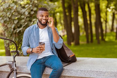 Parkta bankta oturan, cep telefonuyla konuşan ve dışarıda dinlenen yakışıklı afro adam.